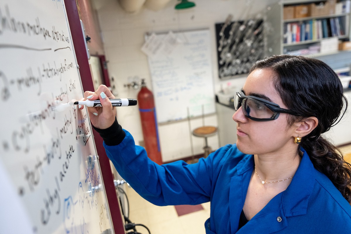 A Villanova graduate chemistry student writes on a board in a lab.