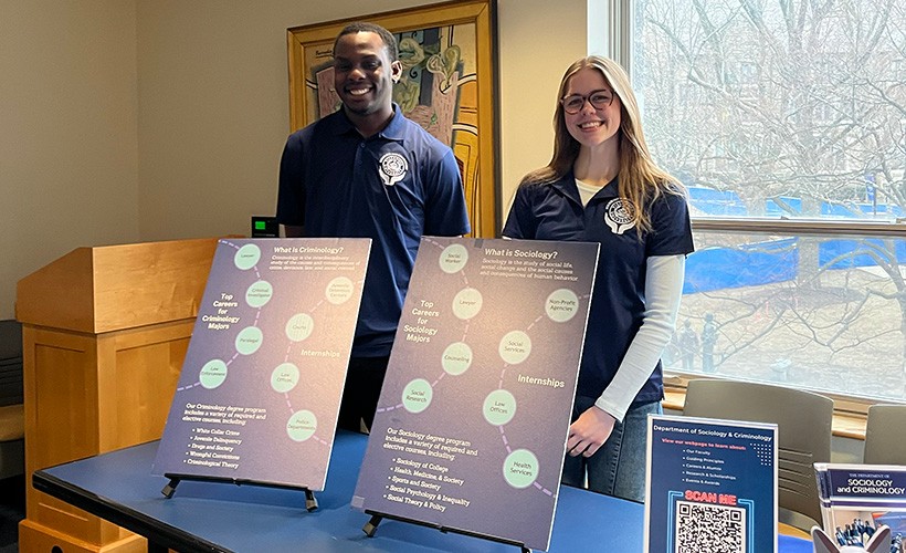 Students stand at a table behind posters about the sociology and criminology majors.