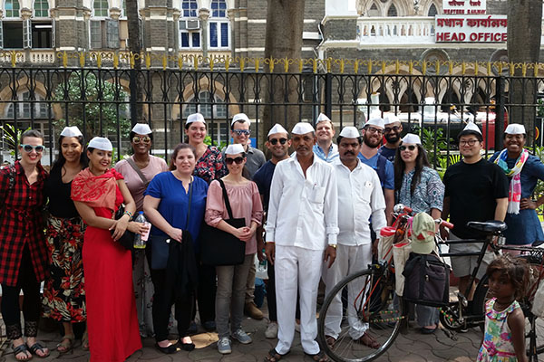 A groups of students stand together outside in a city in India.